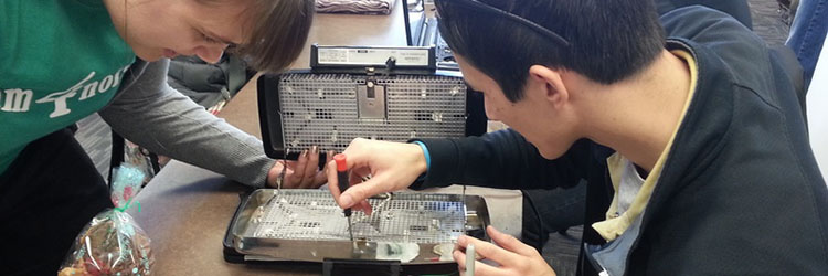 A volunteer fixer helps an attendee repair a waffle iron.